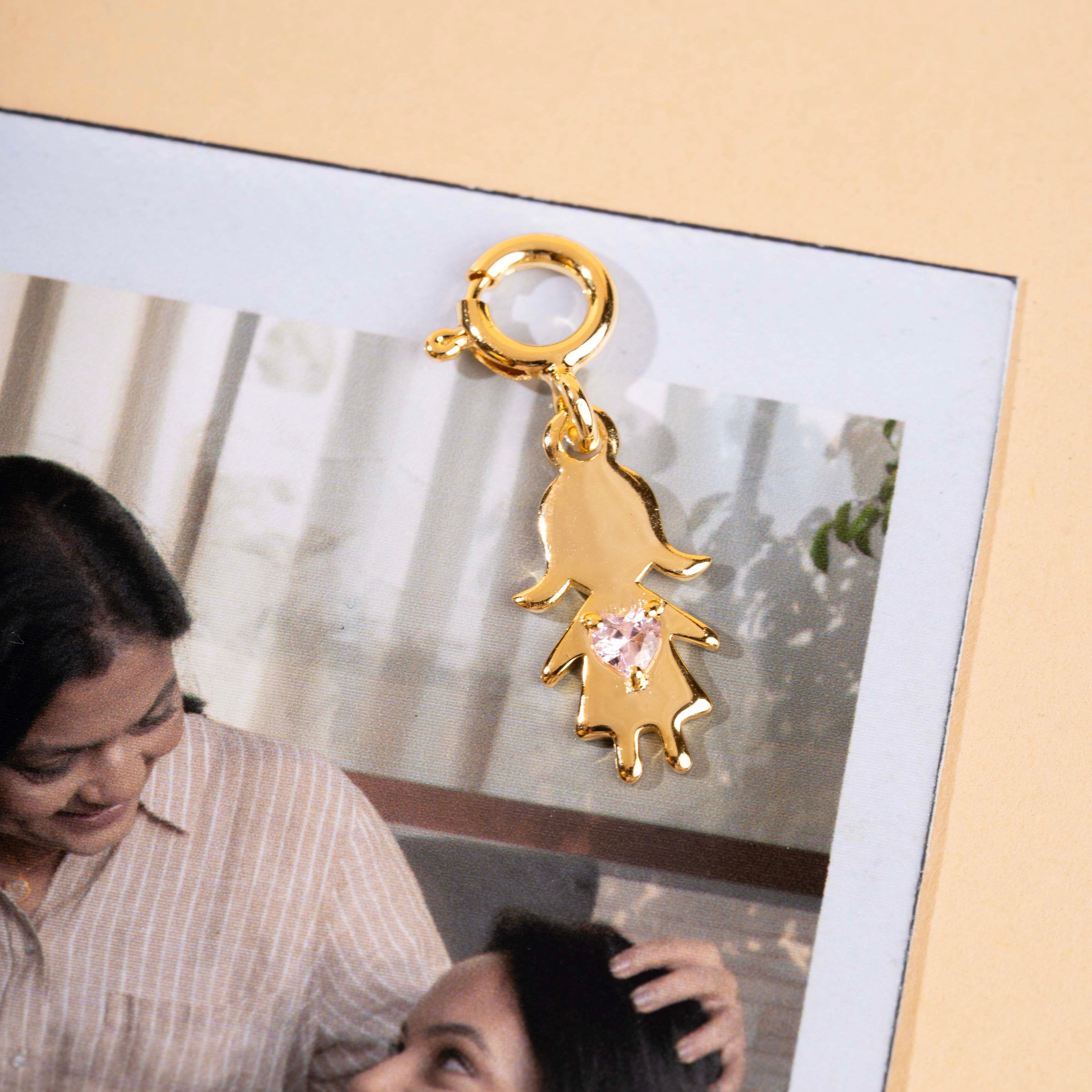 Gold charm with a pink gemstone on a photo of two women smiling.